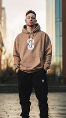 Man wearing a brown hoodie with a logo standing in an urban setting