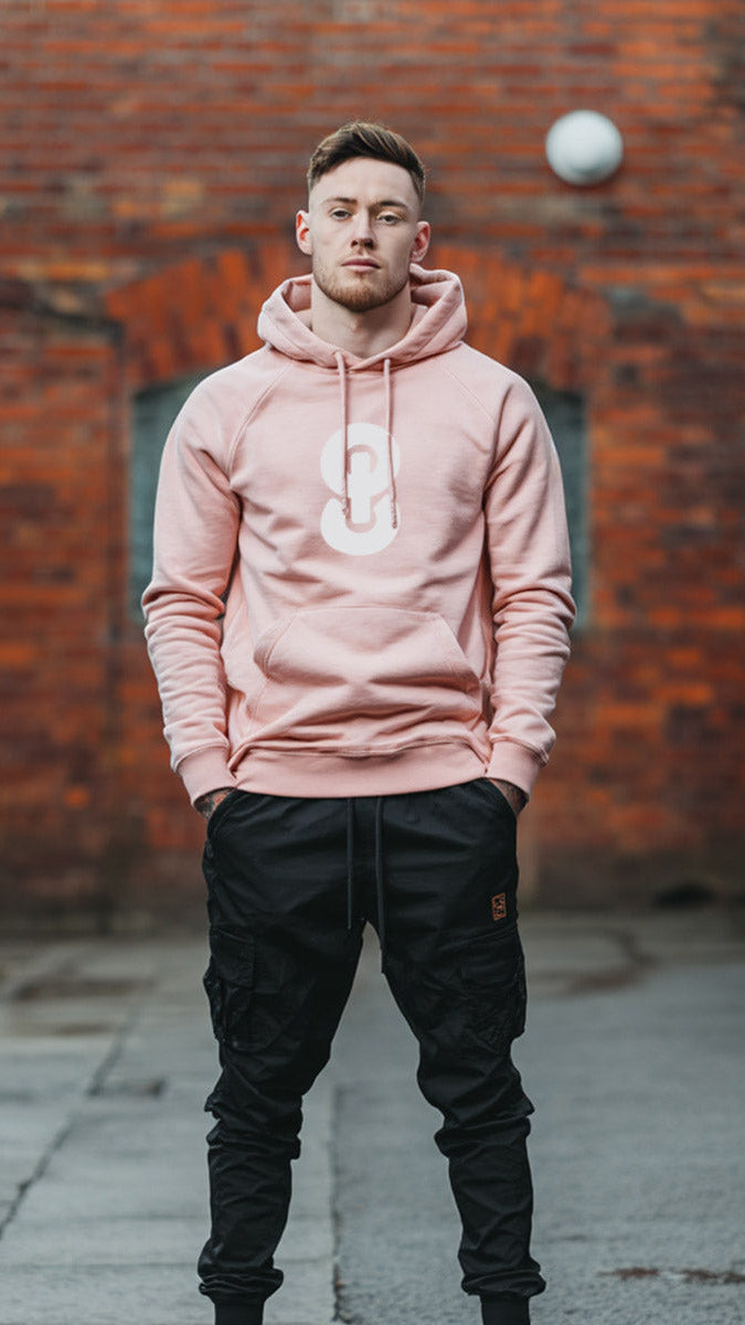 Man wearing a pink hoodie with a logo in front of a brick wall