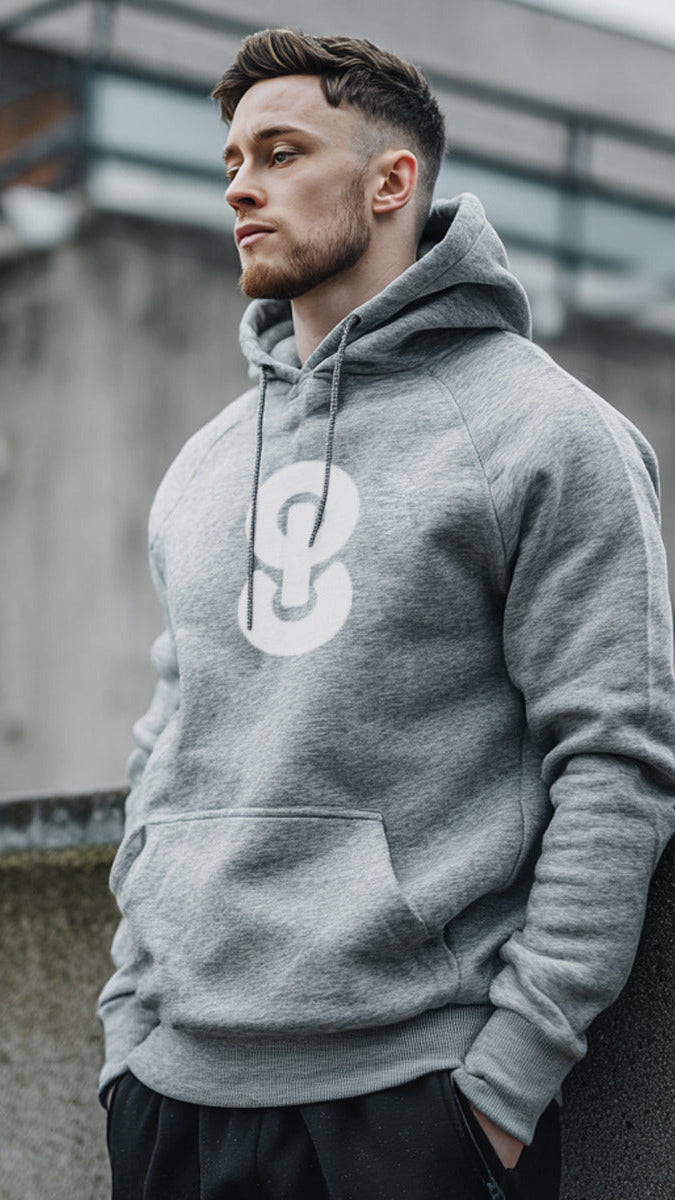 Man wearing a gray hoodie with a logo, standing against an urban background.
