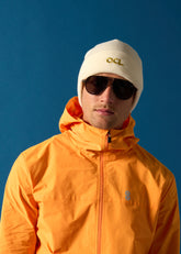 Person wearing an orange OCL jacket and white beanie with 'OCL' logo against a blue background