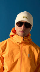 Person wearing an orange OCL jacket and white beanie with 'OCL' logo against a blue background