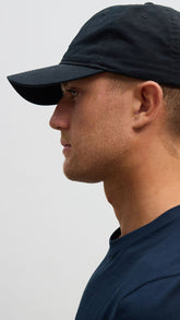 A person wearing a black baseball cap with white embroidery on the front.