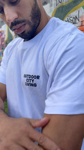 Person wearing a white t-shirt with 'Outdoor City Living' text, standing against a colorful mural.