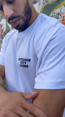 Person wearing a white t-shirt with 'Outdoor City Living' text, standing against a colorful mural.