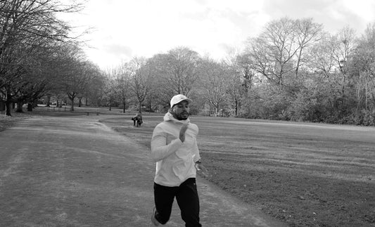 Jordan running in a park in London, black and white image, wearing OCL white cap, light blue windbreaker and OCL tracksuit bottoms