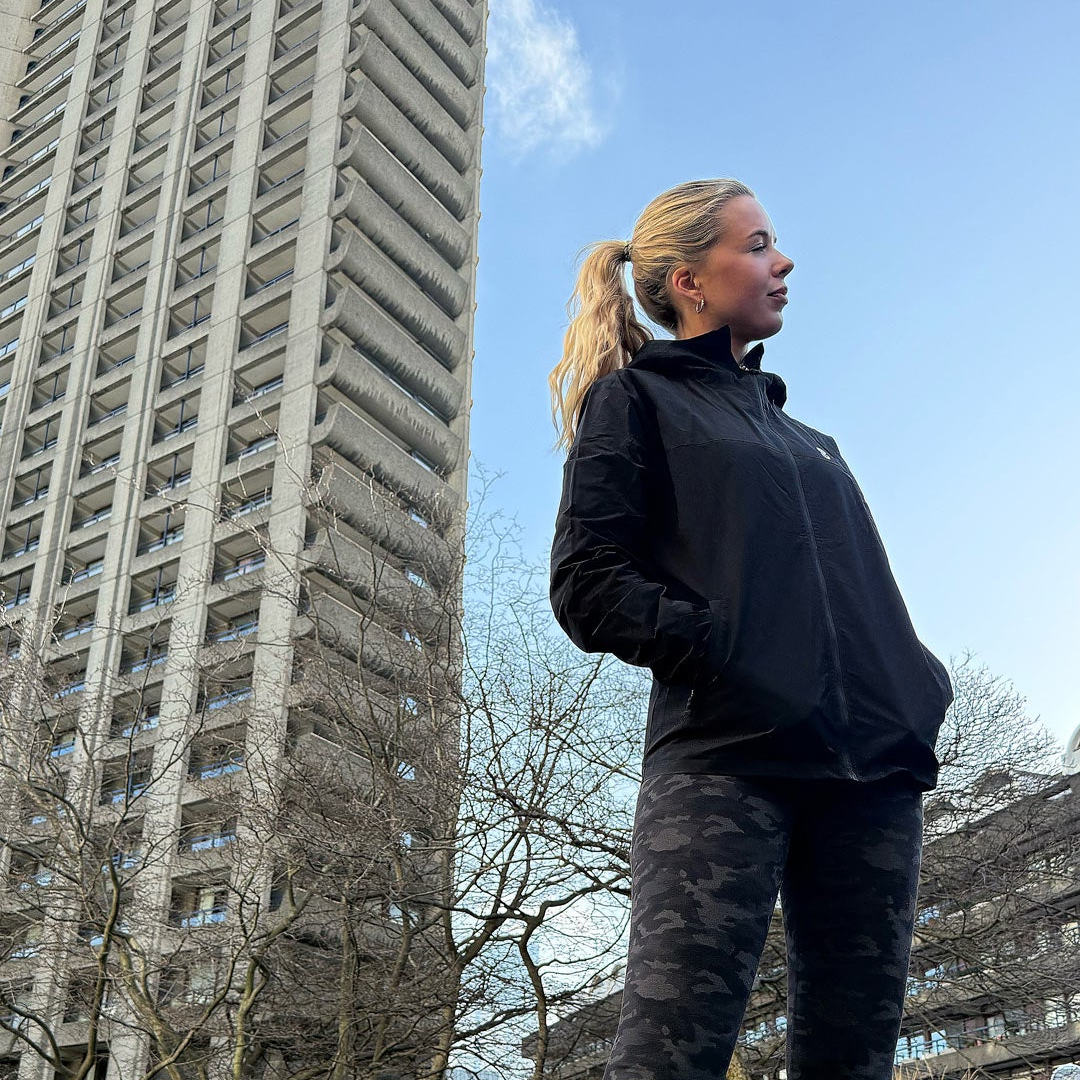 Person wearing a black OCL jacket and camouflage pants standing in front of a tall building.