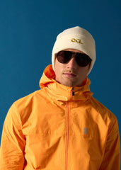 Person wearing an orange OCL jacket and white beanie with 'OCL' logo against a blue background